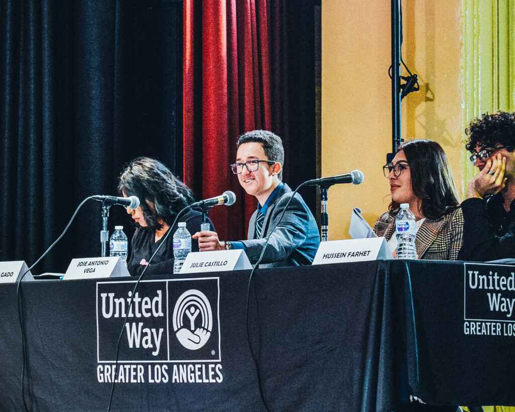 A panel of three young students sit in front of microphones