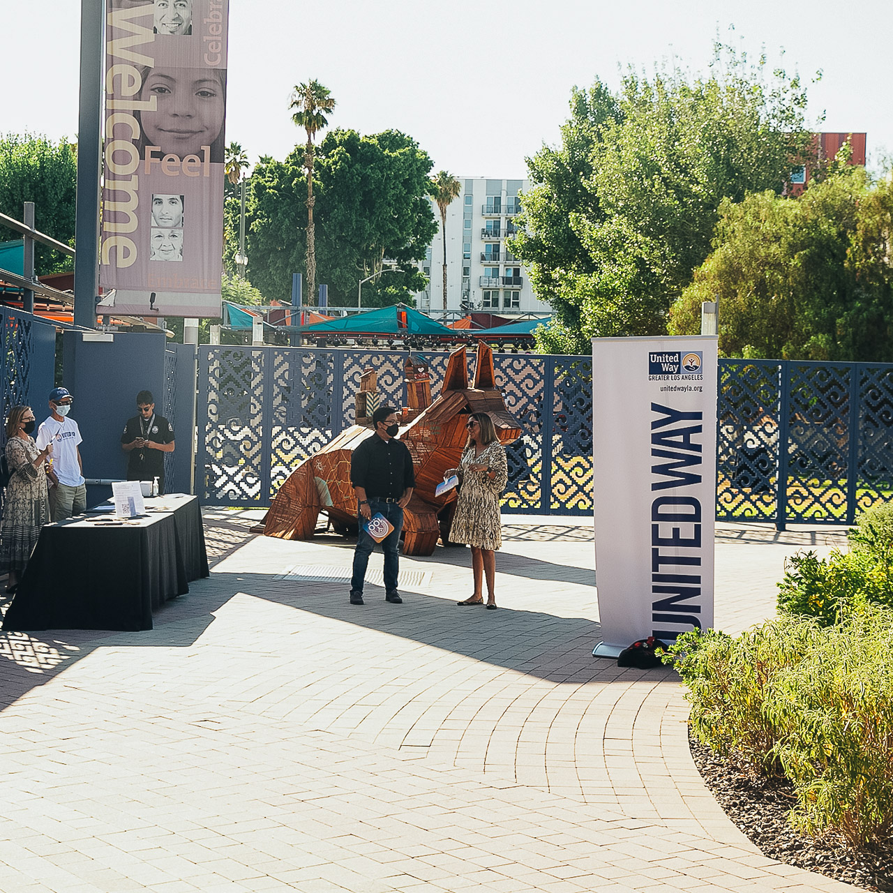 People talk to each other in a sunny courtyard. There's a sign that says United Way of Greater L.A.