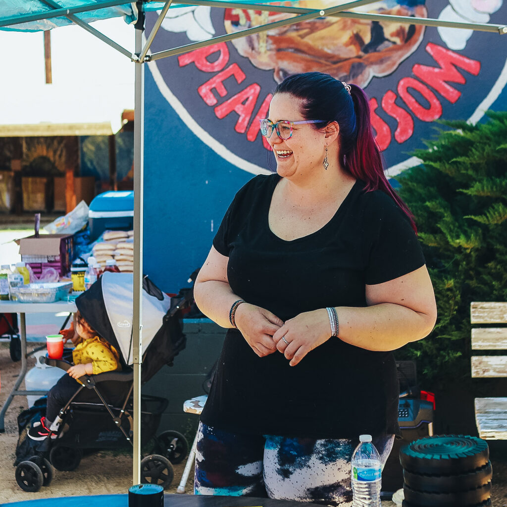 Woman with glasses, black shirt and dark hair stands with her hands folded.