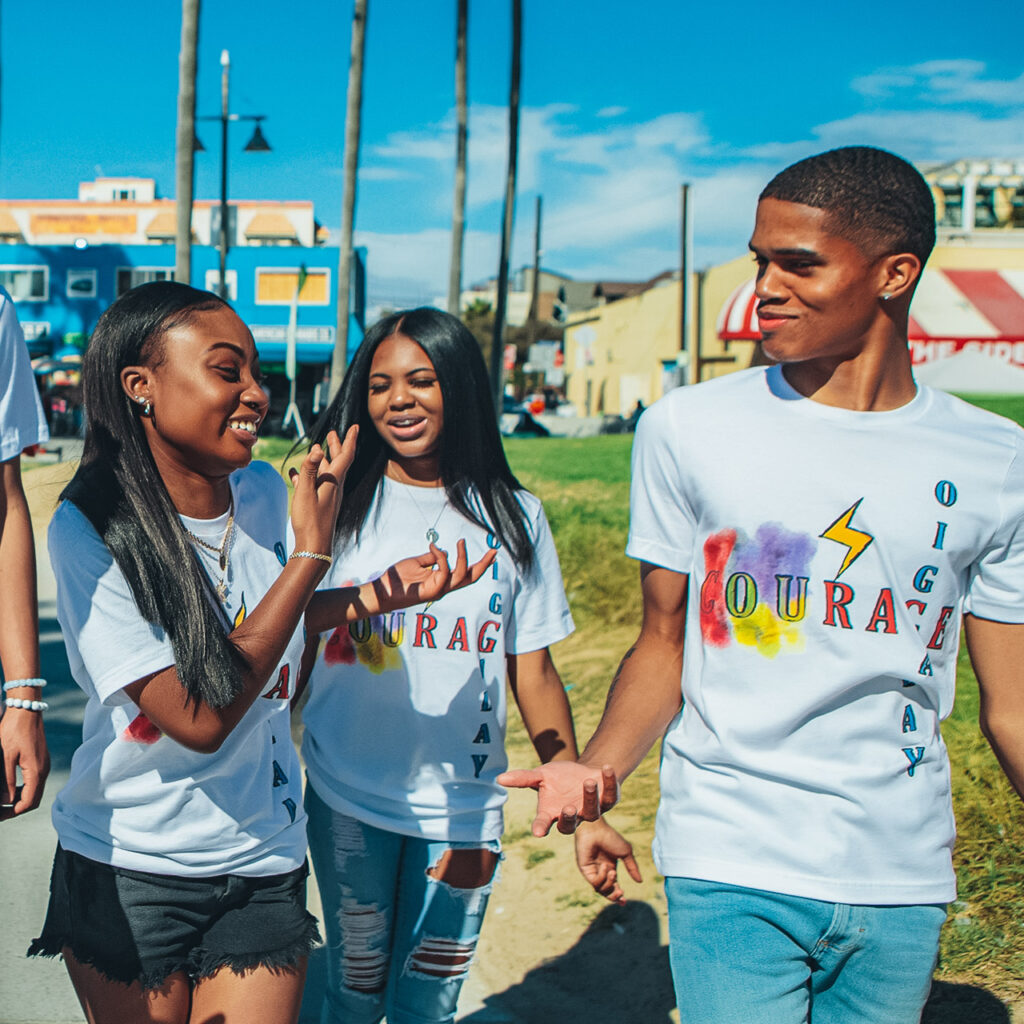 Three young people walking and laughing together at an outdoor event. It's a sunny day and the sky is clear blue.