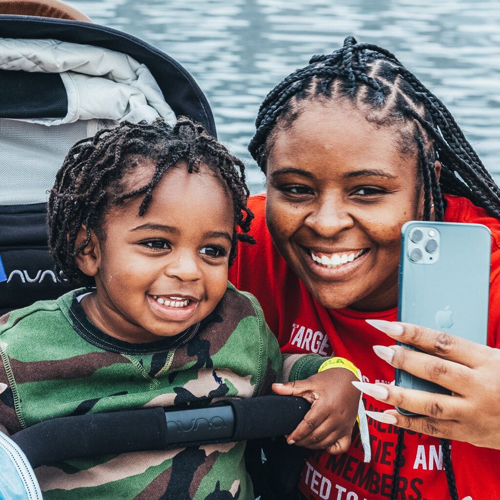 Woman of color smiles with her child into her camera phone taking a selfie.