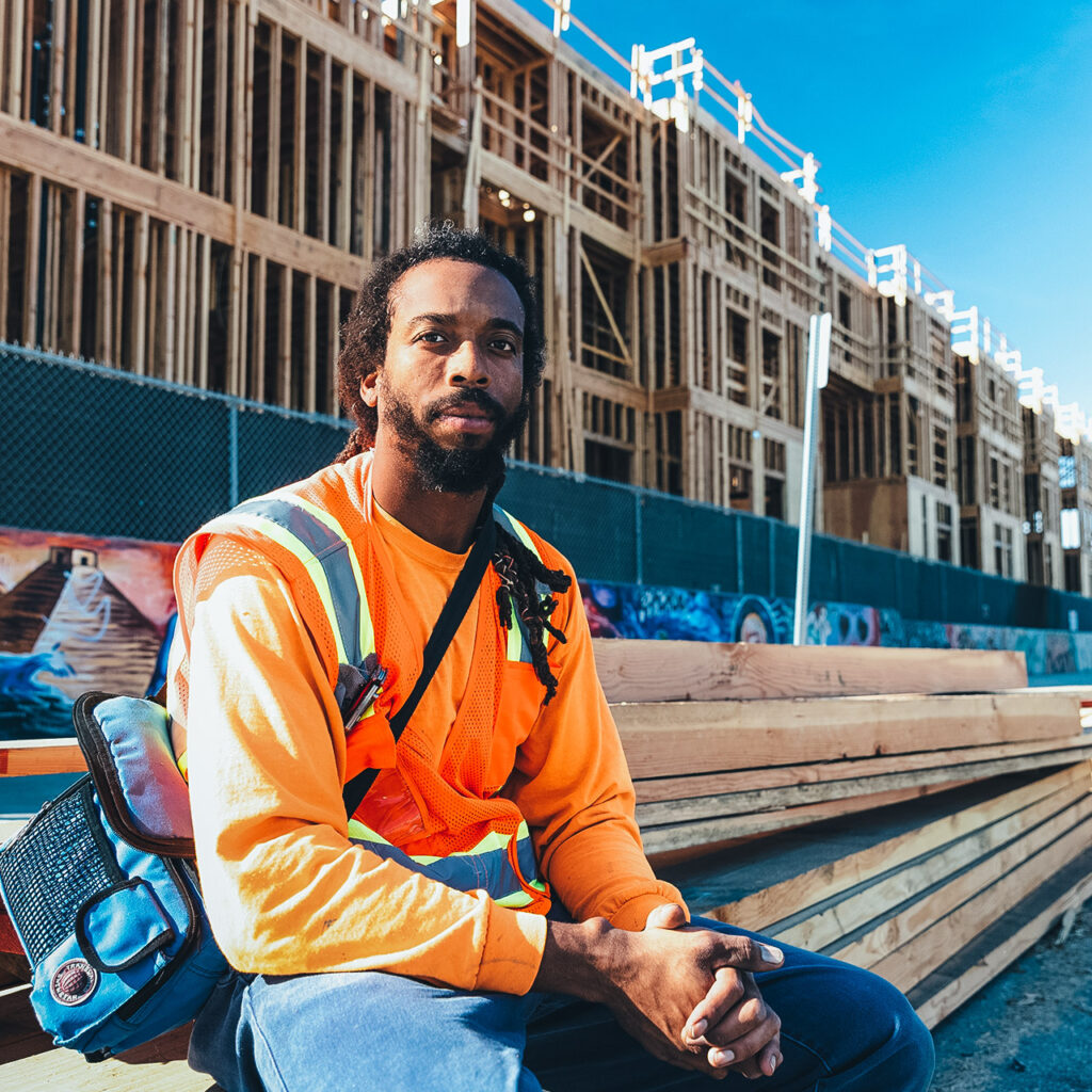 Man wearing a reflector vest sits in front of a new housing development project.