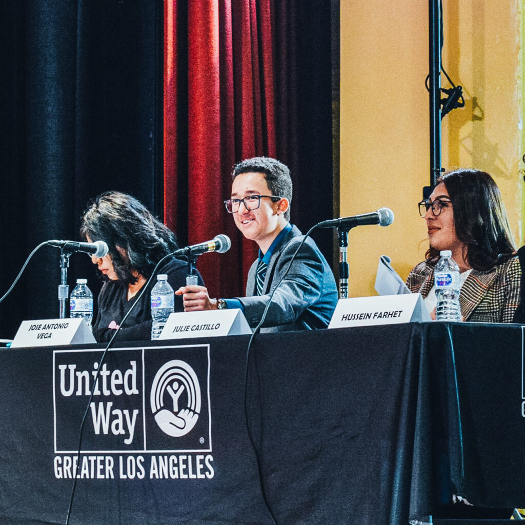 A panel of three young students sit in front of microphones