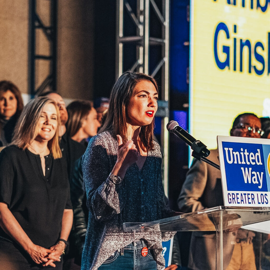 A woman speaks at a podium on a stage. A sign on the podium says United Way of Greater L.A.
