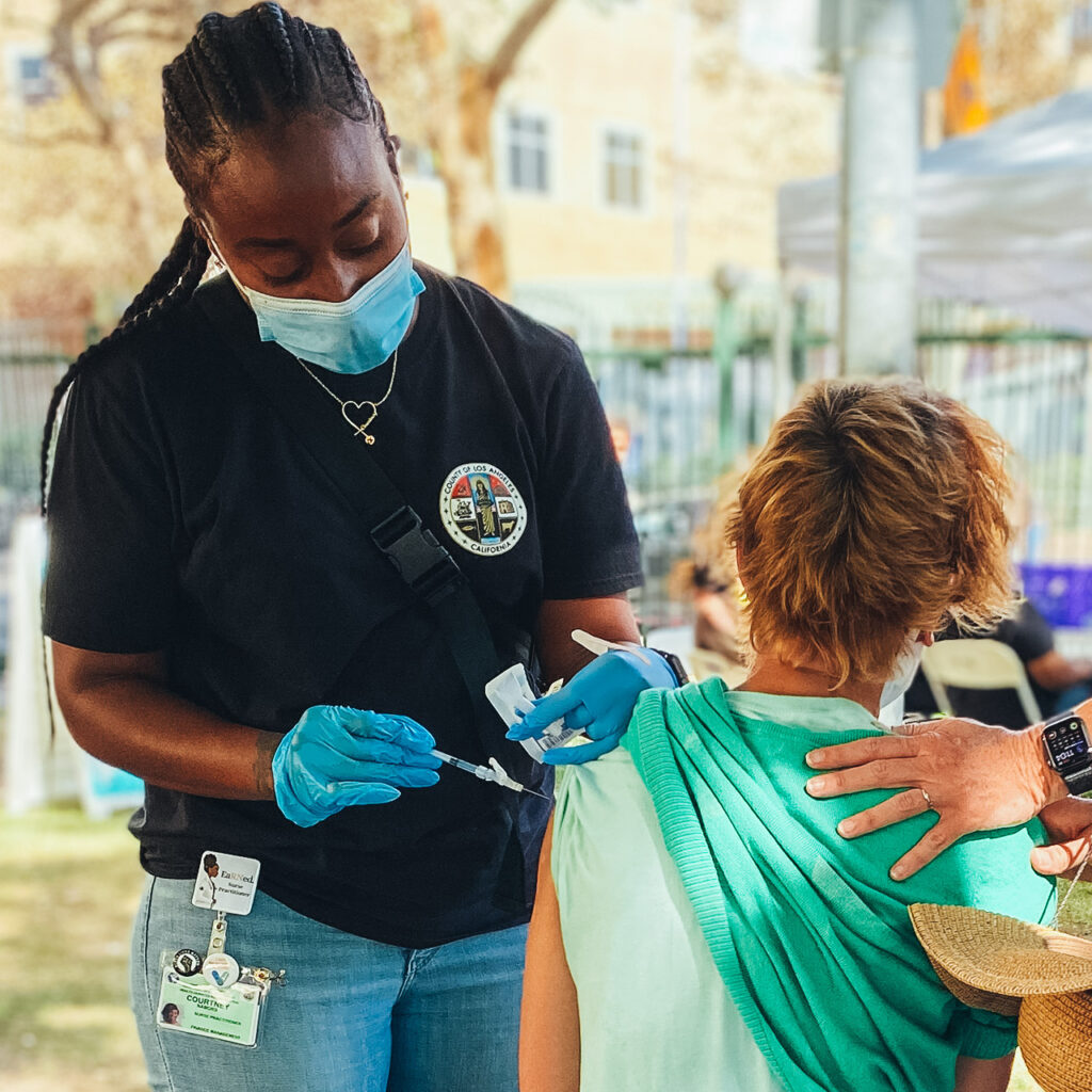 Healthcare worker administers a vaccine while a supportive hand supports the patient