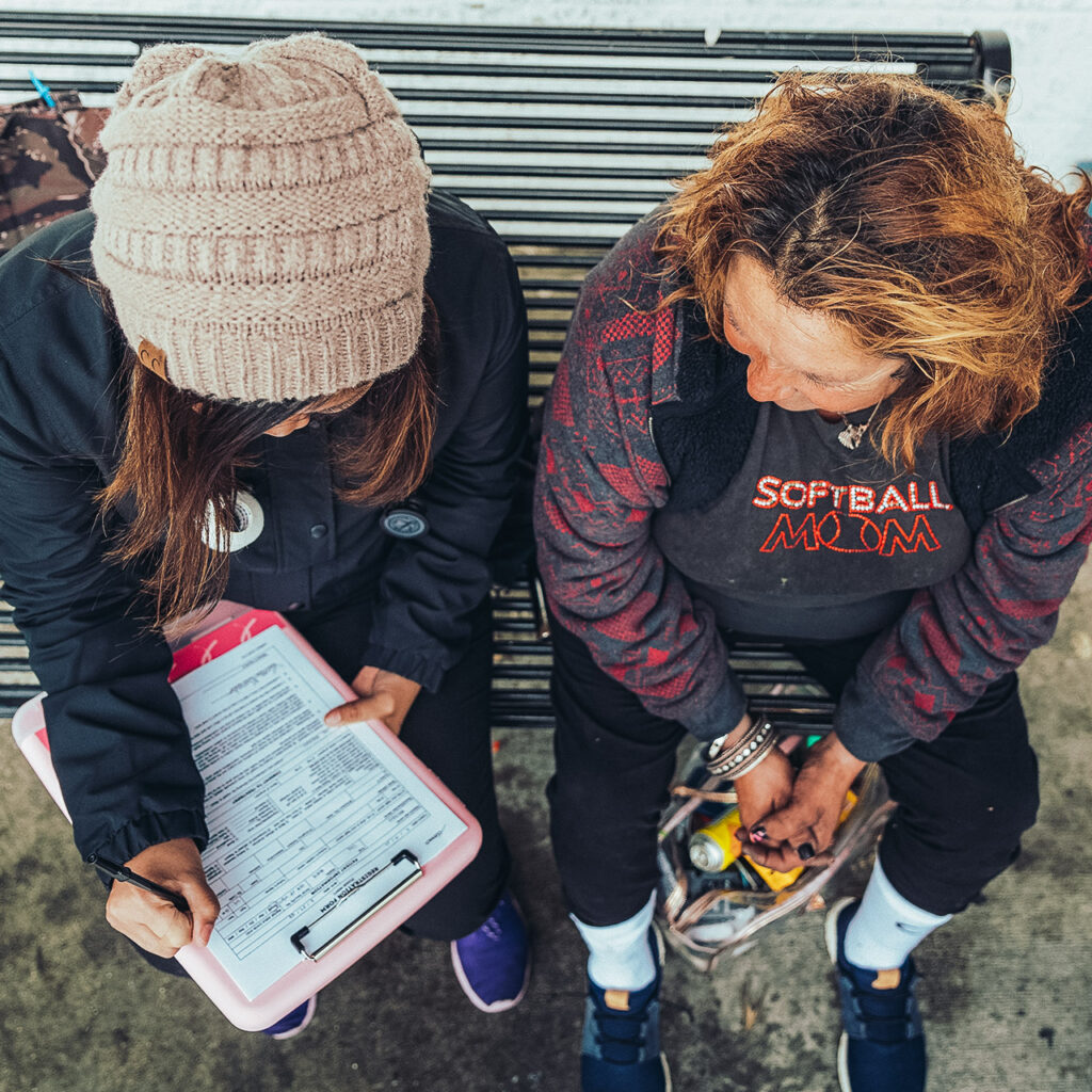 An outreach worker interviews a patient to provide medical care—taking notes on a clipboard